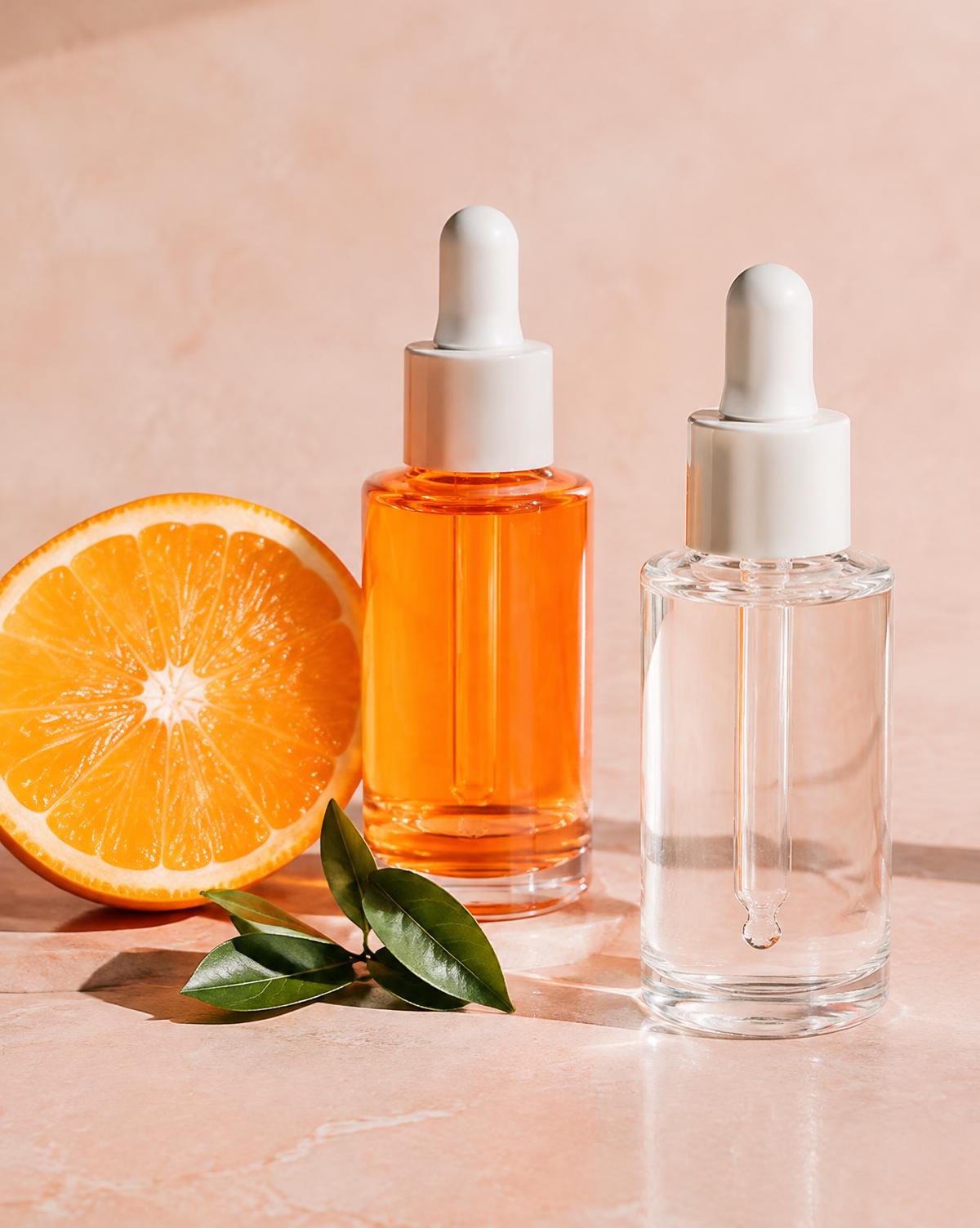 Orange vitamin C serum and clear serum beside an orange