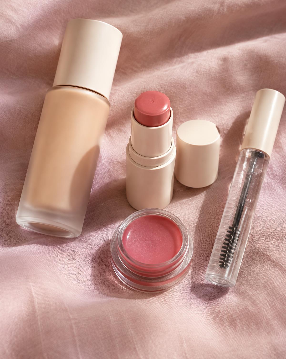 Skin tint, cream blush stick, lip balm and brow gel on pink linen
