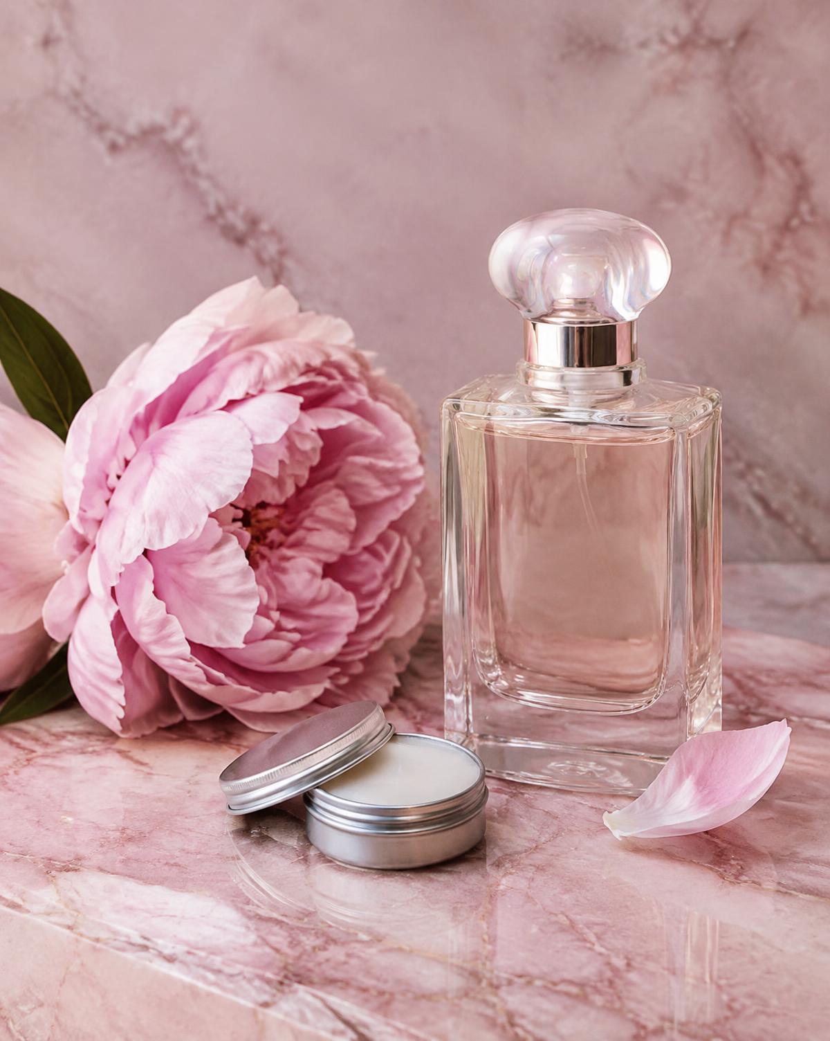 Glass perfume bottle, balm tin and peony on pink marble