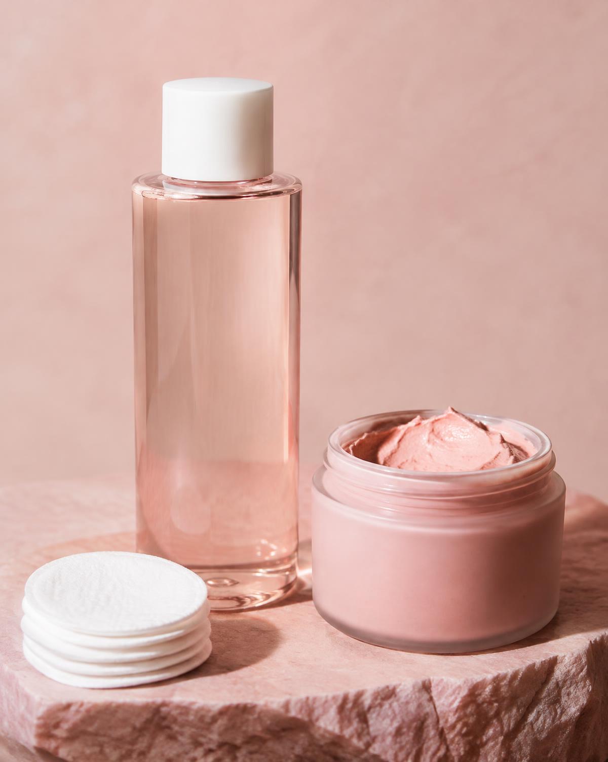 Toner bottle, clay mask jar and cotton pads on pink stone