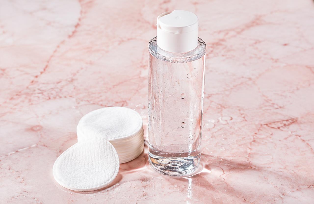 Clear toner bottle with cotton pads on pink marble